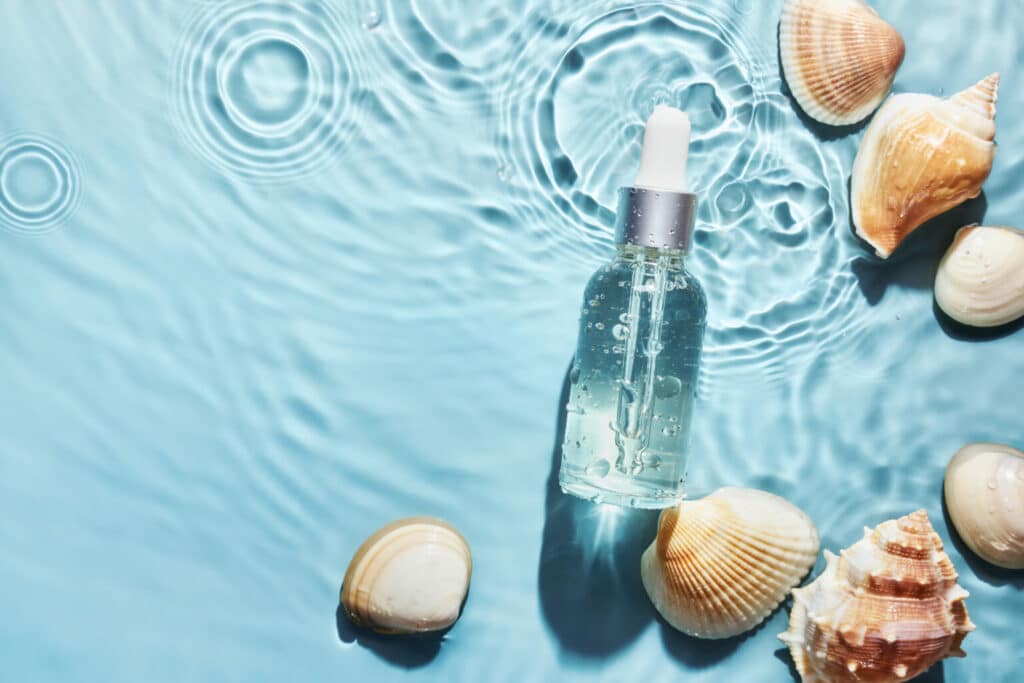 Organic cosmetic with with sea minerals. Skincare cosmetic product and shells on blue water background.