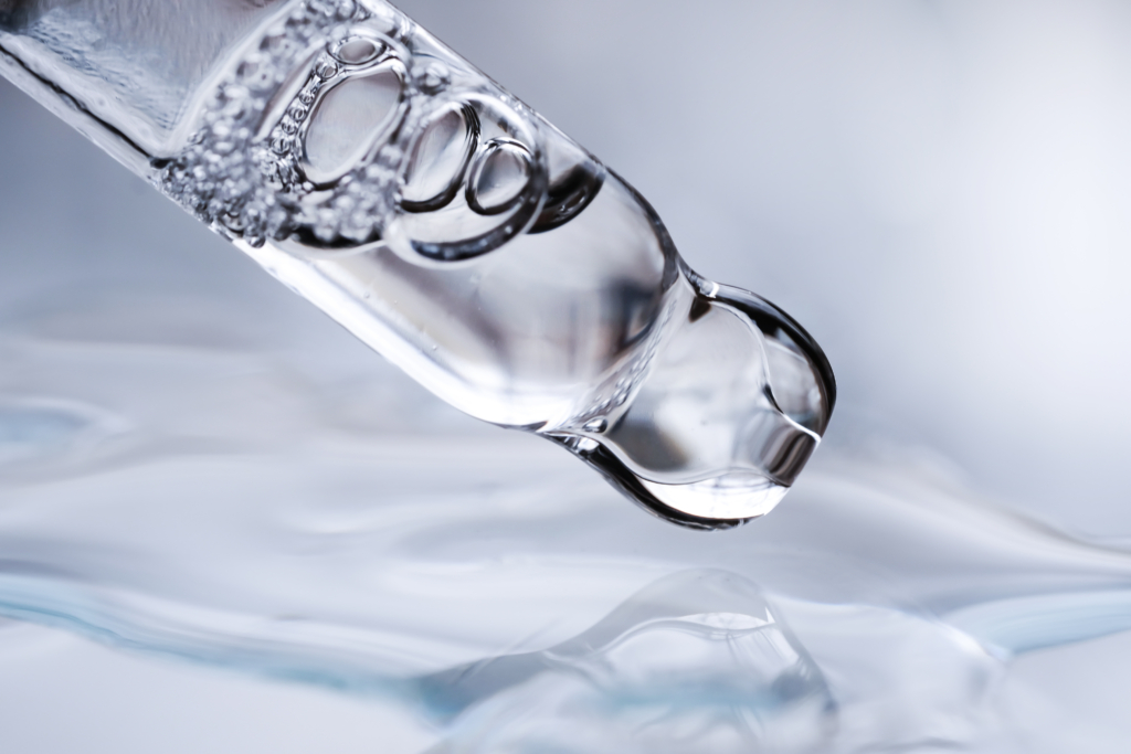 A glass pipette with a close-up of cosmetic liquid on a gray background.